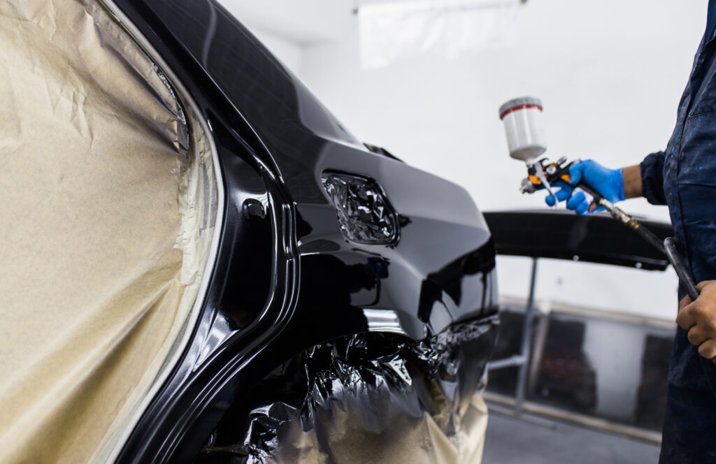 Spray gun refinishing a vehicle body panel